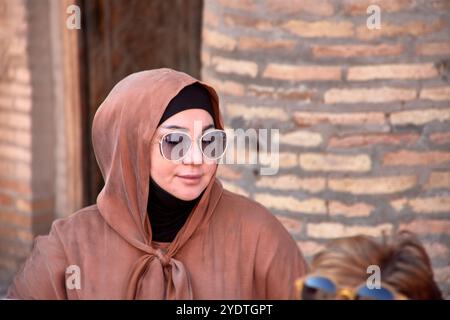 Kihva, Usbekistan; 21. September 2024: Eine stilvolle muslimische Frau in braunem Outfit und passendem Hijab, ergänzt durch eine große Sonnenbrille. Sie läuft Stockfoto