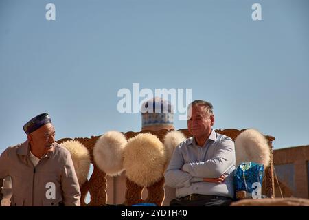 Khiva, Usbekistan; 21. September 2024: Zwei einheimische Männer sitzen auf dem lebhaften Markt von Chiwa, Usbekistan, und verkaufen traditionelle Wollmützen aus Naturstoffen Stockfoto