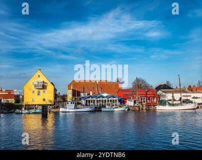 Malerische Küstendörfszene Karrebaeksminde, mit lebhaften gelben und roten Häusern, traditionellen Fischerbooten und einem ruhigen blauen Meer unter einer klaren Ske Stockfoto