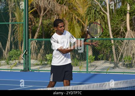 Randheli, Malediven - 24. Februar 2014: Ein asiatischer Indianer spielt Tennis auf einem tropisch blauen Tennisplatz. Stockfoto
