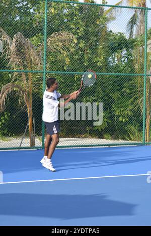Randheli, Malediven - 24. Februar 2014: Ein asiatischer Indianer spielt Tennis auf einem tropisch blauen Tennisplatz. Stockfoto