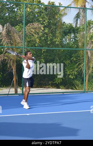 Randheli, Malediven - 24. Februar 2014: Ein asiatischer Indianer spielt Tennis auf einem tropisch blauen Tennisplatz. Stockfoto