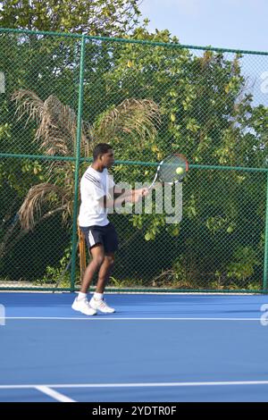 Randheli, Malediven - 24. Februar 2014: Ein asiatischer Indianer spielt Tennis auf einem tropisch blauen Tennisplatz. Stockfoto