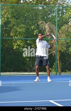 Randheli, Malediven - 24. Februar 2014: Ein asiatischer Indianer spielt Tennis auf einem tropisch blauen Tennisplatz. Stockfoto