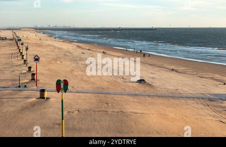 Menschen, die beim Sonnenuntergang am öffentlichen Strand in Scheveningen spazieren gehen. Kitesurfer segeln im Hintergrund. Den Haag, Niederlande - 10. Juli 2024: Menschen, die bei Sonnenuntergang am öffentlichen Strand in Scheveningen spazieren. Kitesurfer segeln im Hintergrund. Edit netherlands the hauge B97A7388 Stockfoto