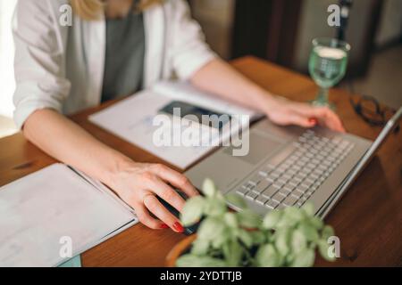 Komfort trifft auf Funktionalität im Home Office-Setup, Frauenhände mit einem Laptop am Tisch bei der Arbeit Stockfoto