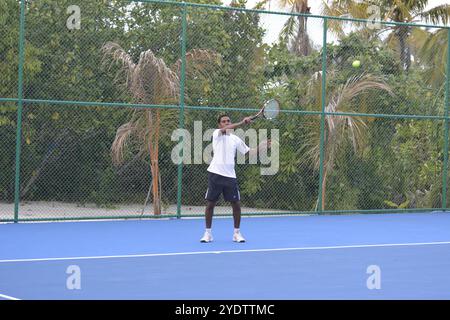 Randheli, Malediven - 24. Februar 2014: Ein asiatischer Indianer spielt Tennis auf einem tropisch blauen Tennisplatz. Stockfoto