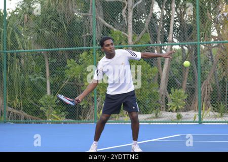 Randheli, Malediven - 24. Februar 2014: Ein asiatischer Indianer spielt Tennis auf einem tropisch blauen Tennisplatz. Stockfoto