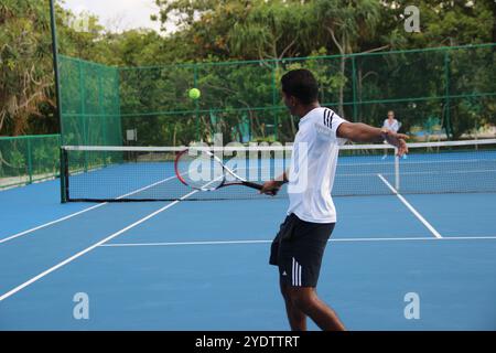 Randheli, Malediven - 24. Februar 2014: Ein asiatischer Indianer spielt Tennis auf einem tropisch blauen Tennisplatz. Stockfoto