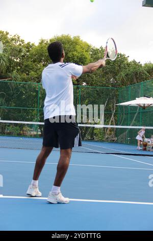 Randheli, Malediven - 24. Februar 2014: Ein asiatischer Indianer spielt Tennis auf einem tropisch blauen Tennisplatz. Stockfoto