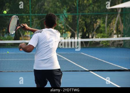 Randheli, Malediven - 24. Februar 2014: Ein asiatischer Indianer spielt Tennis auf einem tropisch blauen Tennisplatz. Stockfoto