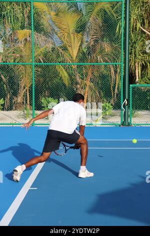 Randheli, Malediven - 24. Februar 2014: Ein asiatischer Indianer spielt Tennis auf einem tropisch blauen Tennisplatz. Stockfoto