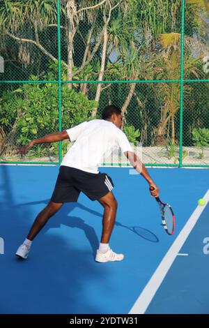Randheli, Malediven - 24. Februar 2014: Ein asiatischer Indianer spielt Tennis auf einem tropisch blauen Tennisplatz. Stockfoto