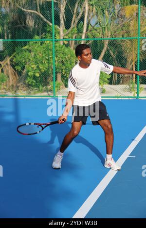 Randheli, Malediven - 24. Februar 2014: Ein asiatischer Indianer spielt Tennis auf einem tropisch blauen Tennisplatz. Stockfoto