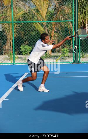 Randheli, Malediven - 24. Februar 2014: Ein asiatischer Indianer spielt Tennis auf einem tropisch blauen Tennisplatz. Stockfoto