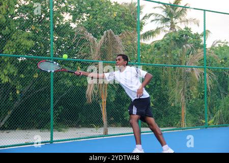Randheli, Malediven - 24. Februar 2014: Ein asiatischer Indianer spielt Tennis auf einem tropisch blauen Tennisplatz. Stockfoto