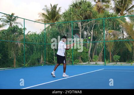 Randheli, Malediven - 24. Februar 2014: Ein asiatischer Indianer spielt Tennis auf einem tropisch blauen Tennisplatz. Stockfoto