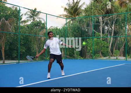 Randheli, Malediven - 24. Februar 2014: Ein asiatischer Indianer spielt Tennis auf einem tropisch blauen Tennisplatz. Stockfoto