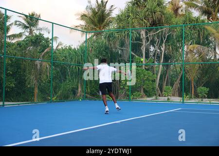 Randheli, Malediven - 24. Februar 2014: Ein asiatischer Indianer spielt Tennis auf einem tropisch blauen Tennisplatz. Stockfoto