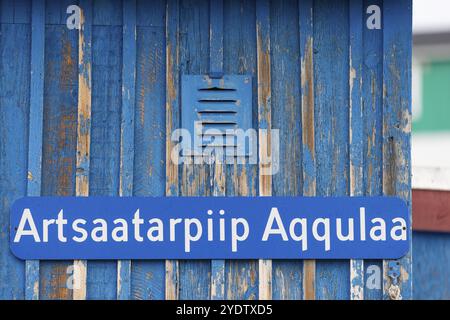 Ein blaues Schild mit einem grönländischen Straßennamen auf einer wetterdurchfluteten Holzwand, abgelegene Arctic Inuit Siedlung von Ittoqqortoormiit, Scoresbysund Stockfoto