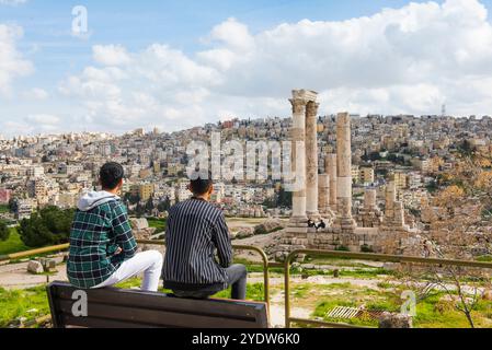 Zwei junge jordanische Männer sitzen auf einer Bank gegenüber dem Tempel des Herkules in der Zitadelle von Amman (Jabal al-Qal'a), Amman, Jordanien Stockfoto