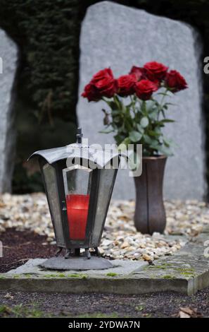 Grablaterne mit brennender Kerze auf einem Grab vor einem Strauß roter Rosen in einem verschwommenen Hintergrund Stockfoto