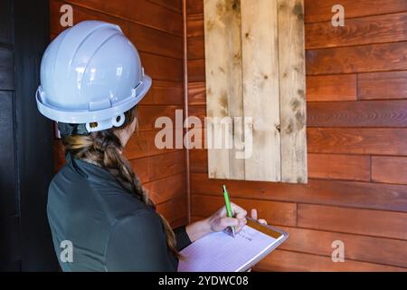 Nahansicht der Inspektorin, die sich während der Innenraumluftqualitätskontrolle Notizen macht, auf der Suche nach Schimmel- oder Pilzproblemen an den Holzwänden Stockfoto