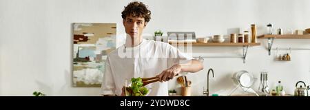 Ein hübscher junger Mann kreiert einen Salat, der ein gesundes Leben in einer eleganten Küche verkörpert. Stockfoto