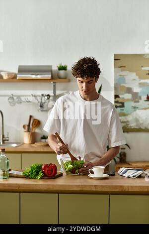 Ein gutaussehender junger Mann bereitet geschickt einen gesunden Salat in einer modernen Küche zu, der einen lebendigen Lebensstil annimmt. Stockfoto