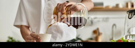 Ein junger Mann gießt vorsichtig frischen Kaffee in eine kleine Tasse in seiner warmen Küche. Stockfoto