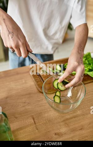 Ein junger Mann schneidet gekonnt Gurken für einen gesunden Salat in einer modernen Küche. Stockfoto