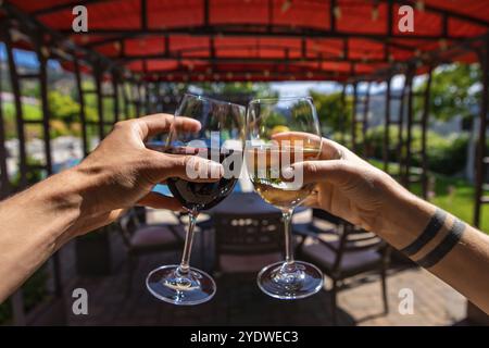 Zwei Hände genießen und rösten Rotwein- und Weißweingläser selektiver Fokus, Restaurants im Freien Sitzplätze während sonnigem Sommertag Hintergrund Stockfoto