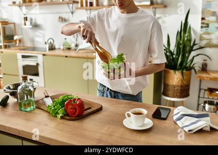 In einer modernen Küche wirft ein junger Mann gekonnt frische Zutaten, um einen lebendigen Salat für eine gesunde Mahlzeit zu kreieren. Stockfoto