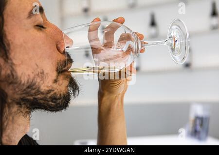Kaukasische Mann trinken und schmeckt ein Glas Weißwein mit geschlossenen Augen, Gesicht Seite selektiven Fokus Nahaufnahme, innen weiß Design kopieren Raum Stockfoto