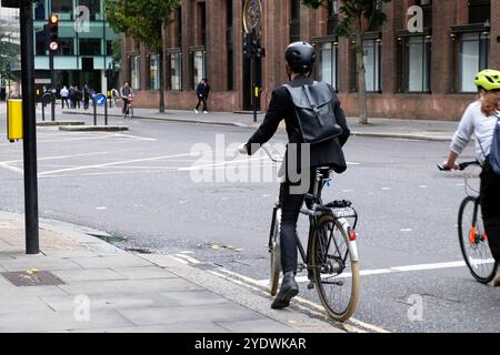 Rückansicht der Person, die schwarze Kleidung trägt, Rucksackhelm, die auf dem Fahrrad wartet, bis die Ampel geändert wird City of London England Großbritannien KATHY DEWITT Stockfoto