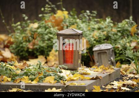 Herbstblätter liegen auf einem Grab mit einer Grablaterne Stockfoto