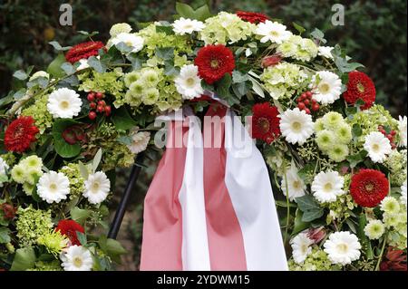 Ein Trauerkranz auf einem Rahmen mit bunten Blumen und einer rot-weißen Schleife Stockfoto