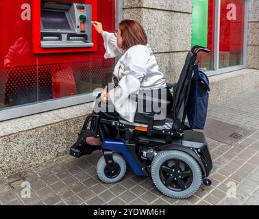 Frau im Rollstuhl, die einen Geldautomaten auf der Straße benutzt Stockfoto