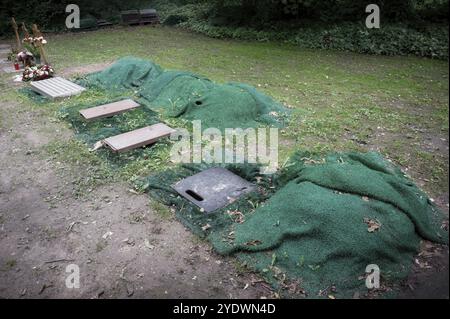 Mehrere Urnengräber, die mit grünen Matten gesäumt und mit Schutzdeckeln ausgestattet sind, die für die Beerdigung auf einem Friedhof für die Armen vorbereitet wurden Stockfoto