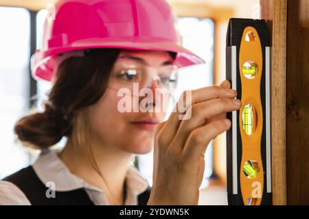 Selektiver Fokus und Nahaufnahme der Wasserwaage auf der Hand der Frau mit ihrem attraktiven Gesicht im Hintergrund. Architektin bei der Qualitätskontrolle Stockfoto