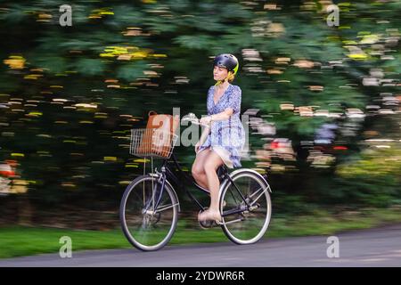 Eine Frau fährt mit ihrem Pendler-Push-Bike auf einem Radweg durch den Jardin Eglise in Genf, Schweiz. Stockfoto