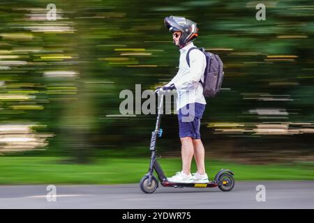 Ein Mann fährt mit seinem Elektroroller auf einem Radweg durch den Jardin Eglise in Genf, Schweiz. Stockfoto