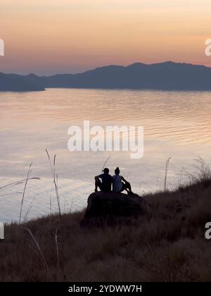Ein Paar, das am Meer sitzt und den Sonnenuntergang betrachtet, Lawa Darat Gili, Indonesien Stockfoto