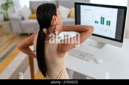 Müde Arbeitnehmerin sitzt am Schreibtisch, Rückenschmerzen leiden, Frau starke Rückenschmerzen, falsche Haltung Stockfoto