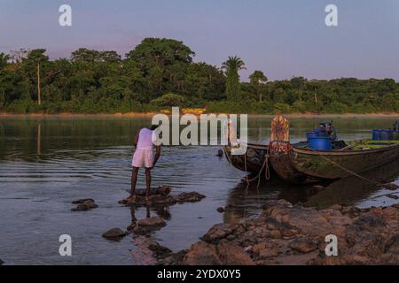 Morgens Ruhe im Stoelmans Eiland, Suriname. Farbenfrohe Boote, die an das Ufer gebunden sind, während ein einheimischer Mann seine Zähne mit Flusswasser putzt. Stockfoto