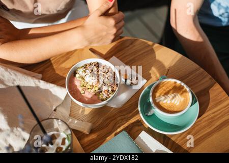 Blick von oben auf zwei Personen, die in der Sommersonne auf einer Terrasse eine Jogurt-Smoothie-Schüssel und Kaffee zum Frühstück trinken wollten Stockfoto