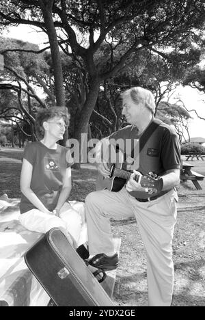 Kaukasisches Seniorenpaar, 50 bis 55 Jahre, entspannte sich an einem Picknicktisch im Myrtle Beach State Park, South Carolina, USA, mit dem Mann, der Gitarre spielt. Stockfoto