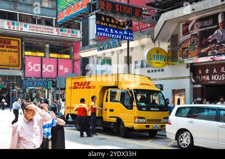 Hongkong, China - 27. April 2009: Ein DHL-Lieferwagen parkt auf einer belebten Straße, umgeben von bunten Schildern und belebten Fußgängern. Stockfoto