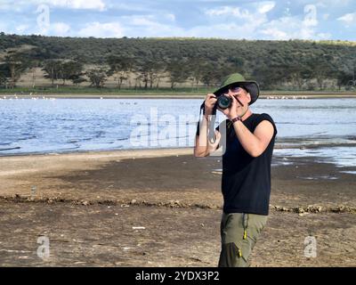 Ein Fotograf mit grünem Hut fotografiert die Savanne auf dem Hintergrund des Lake Nakuru in Kenia. Das Konzept einer afrikanischen Safari in Afrika. A p Stockfoto