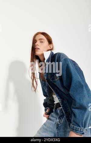 Ein Teenager zeigt sein langes rotes Haar und sein trendiges Denim-Outfit in einem hellen Studio-Ambiente. Stockfoto